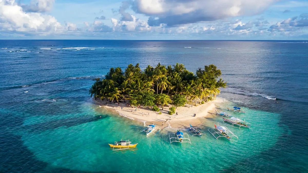 Aerial view of a small palm-covered island in Siargao surrounded by turquoise water